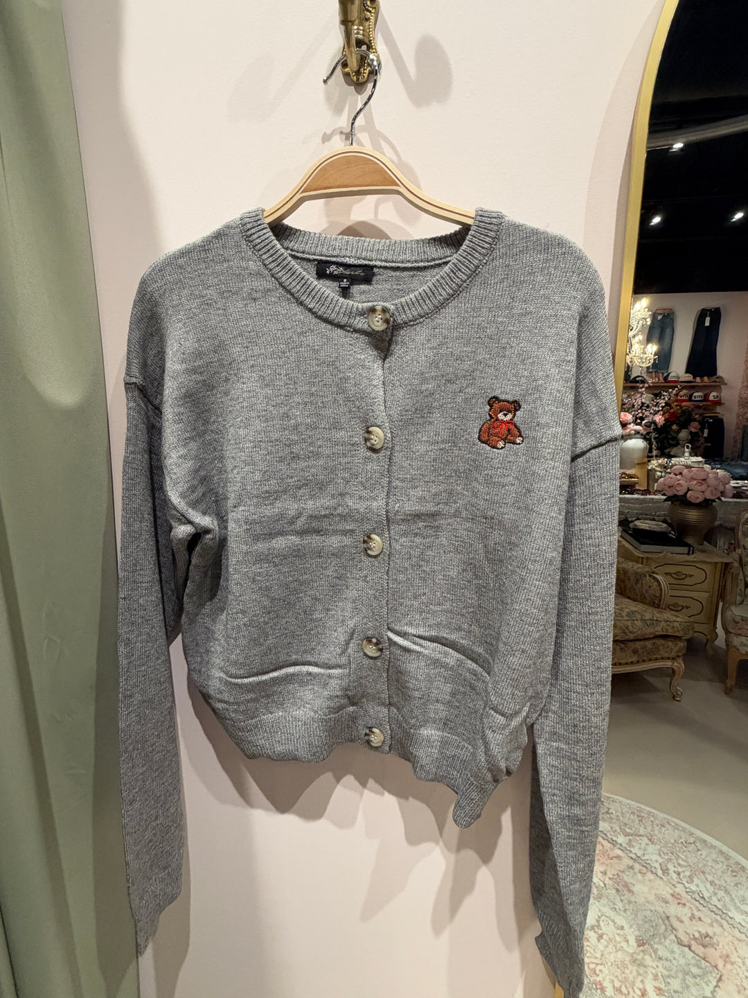 Gray heather knit cardigan with an embroidered teddy bear on the chest and a button front, on a hanger