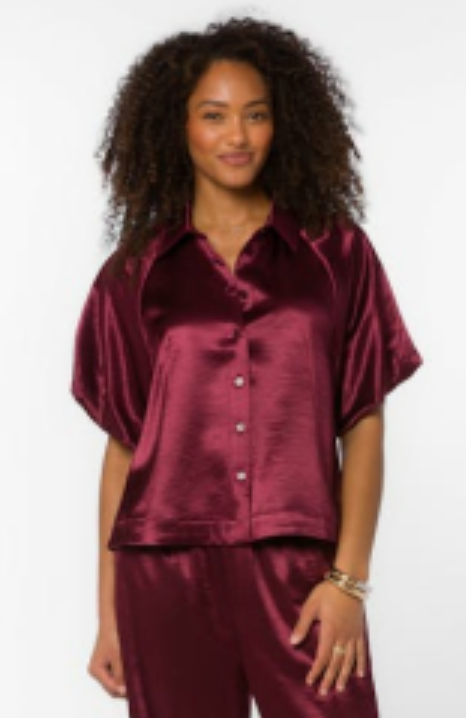 Model wearing a burgundy satin short sleeve button-up top with a camp collar and boxy fit